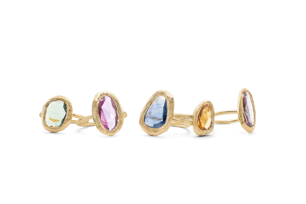 Group shot of handmade 18kt gold rings with rainbow sapphires